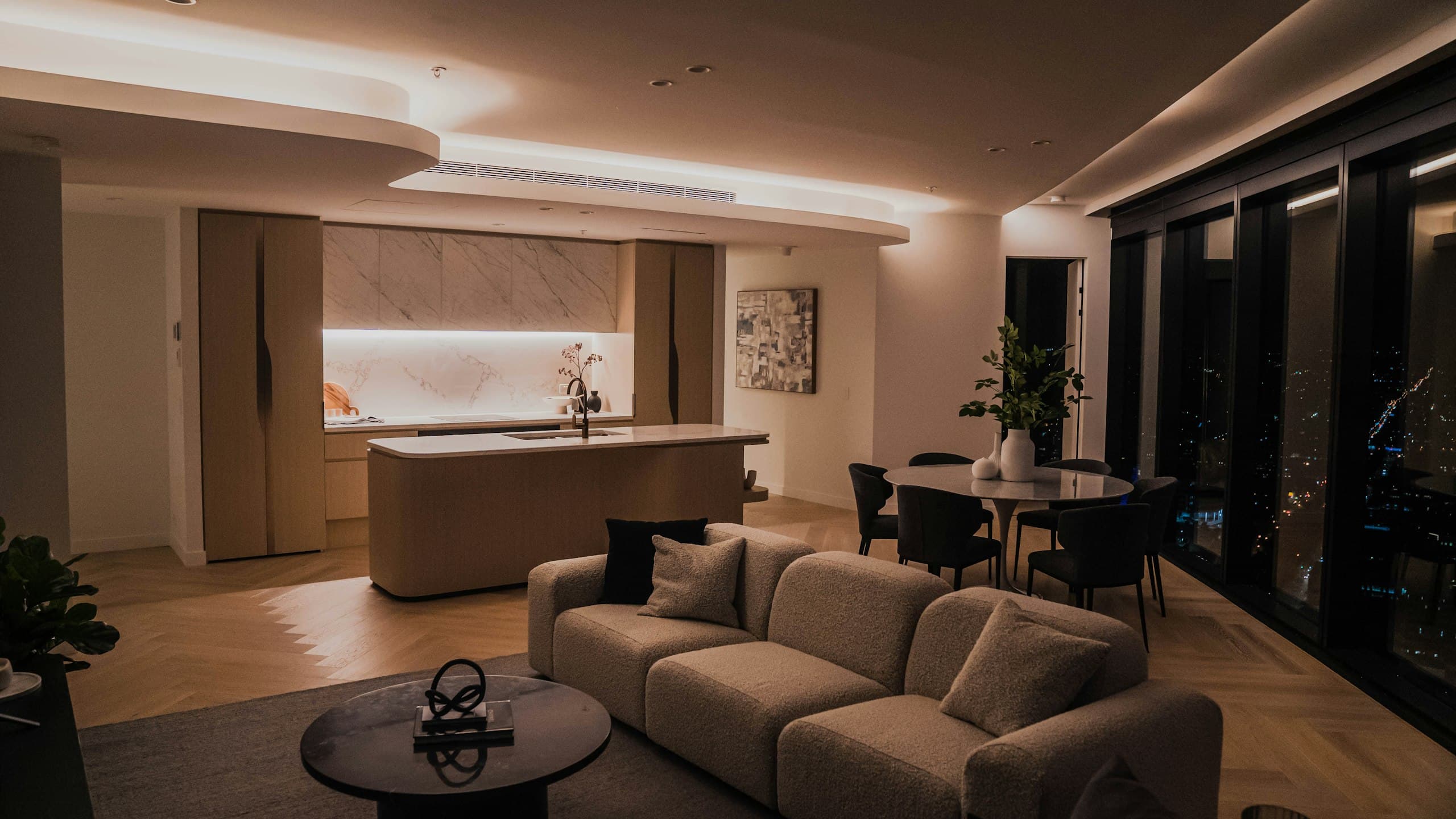 Open living room and kitchen at night with warm cove lighting and city lights through the windows